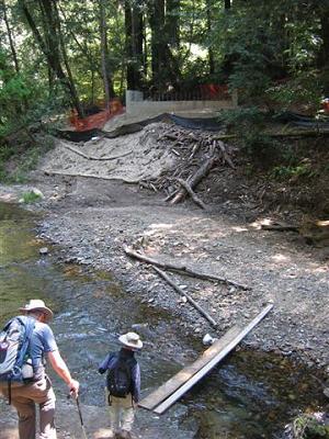 hikers preparing to cross stream on two wood planks placed side by side