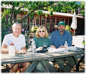 John Flinn and companions at a picnic table, tasting a bottle of wine