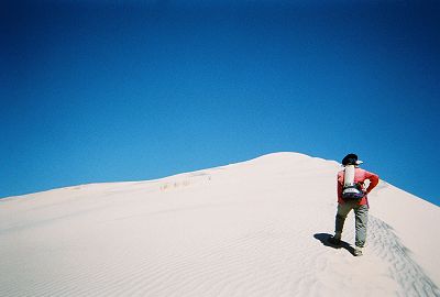 hiker climbing a barren dune ridge