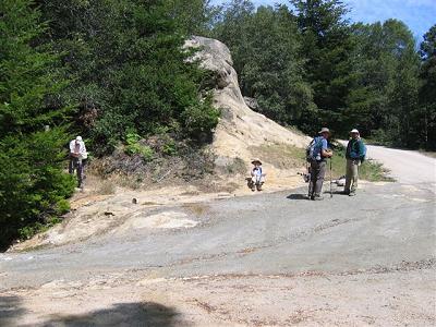 Tom sitting at the edge of the road while others are gathered to talk and one reviews a map