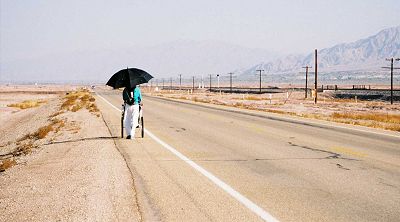 Dinesh Desai walking along the highway under his shade umbrella, pushing his gear on a baby jogger
